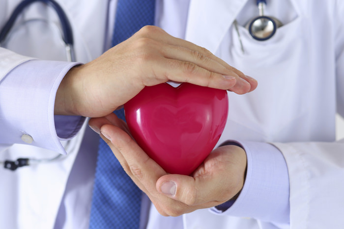 Male medicine doctor hands holding and covering red toy heart closeup. Medical help, cardiology care, health, prophylaxis, prevention, insurance, surgery and resuscitation concept